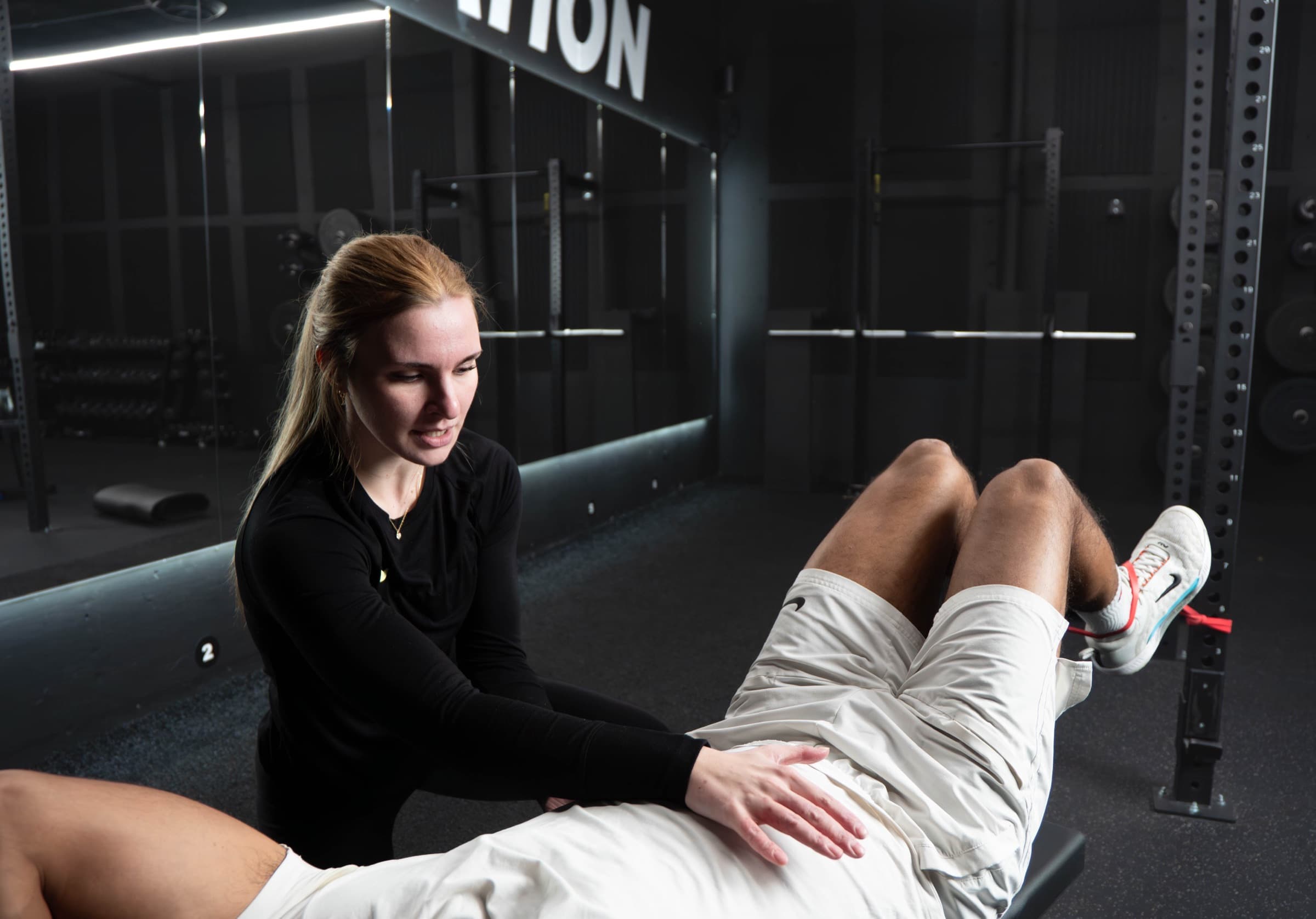 A coach assessing a client lying on a bench in a gym