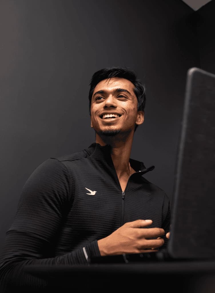 Saran smiling at a laptop in a dark studio